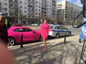 Karolina Pilarczyk stoi na ulicy przed swoim różowym samochodem