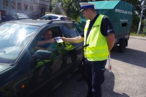 policjant ruchu drogowego wręcza ulotkę kierującemu samochodem