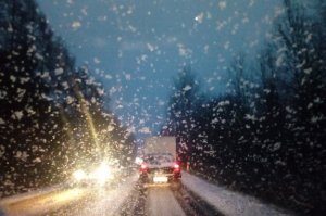 zdjęcie przedstawia ośnieżoną drogę w trakcie zamieci śnieżnej po której poruszają się dwa samochody, droga znajduje się poza obszarem zabudowanym