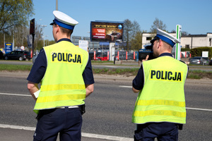 dwóch policjantów w żółtych kamizelkach stoi w pobliżu ruchliwej drogi