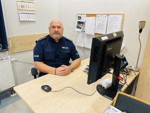 wizerunek policjanta, który siedzi w pomieszczeniu przy biurku