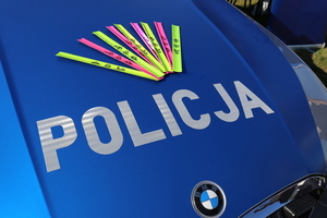 elementy odblaskowe - opaski, w kolorze żółtym i różowym leżą na masce policyjnego radiowozu.