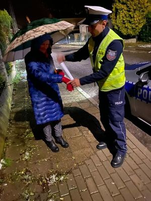 policjant przekazuje element odblaskowy kobiecie, która trzyma parasol