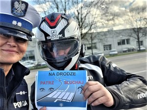 Na zdjęciu policjantka ruchu drogowego i motocyklista w kasku, który trzyma ulotkę z napisem &quot;Na drodze patrz i słuchaj&quot;