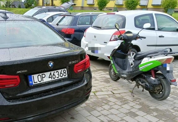 motorower w kolorze zielonym stoi na parkingu miedzy samochodami