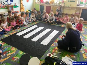 dzieci z przedszkola siedzą na podłodze i słuchają co im mówi policjantka