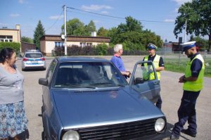 policjanci ruchu drogowego rozmawiają z seniorem, który stoi przy swoim samochodzie