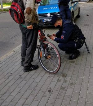 na zdjęciu policjant znajduje się obok roweru w kolorze czarnym, który sprawdza pod katem prawidłowego wyposażenia