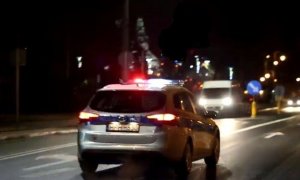 zdjęcie przedstawia radiowóz policyjny z tyłu, jadący ruchliwą drogą w porze wieczorowo-nocnej