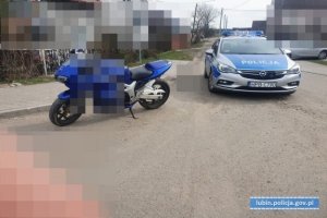 Na zdjęciu widać zaparkowany motocykl w kolorze niebieski i stojący obok policyjny radiowóz.