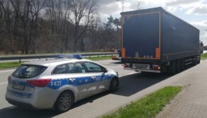 Zdjęcie przedstawia zaparkowany samochód ciężarowy, za którym stoi oznakowany radiowóz