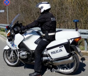 Policjant na motocyklu w białym kolorze stoi na poboczu drogi