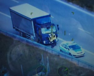 Zdjęcie zrobione z helikoptera widać na nim samochód ciężarowy oraz radiowóz policyjny, przy samochodzie ciężarowym stoi dwóch umundurowanych policjantów.