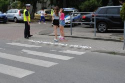 Przed przejściem dla pieszychstoi policjant w białej czapce oraz dwoje dzieci