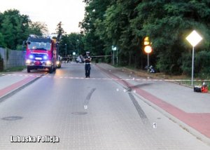 policjanci zabezpieczyli miejsce wypadku zagradzając drogę taśmą, obok stoi samochód straży pożarnej i radiowóz