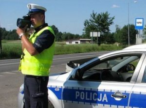 policjant stoi przy radiowozie i kontroluje prędkość radarowym miernikiem prędkości