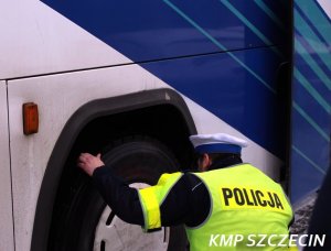 policjant sprawdza koło w autokarze koloru biało-niebieskiego