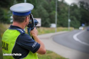 policjant ruchu drogowego stoi przy drodze i trzyma wideorejestrator, którym namierza jadących kierowców