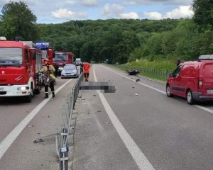 Widok drogi, na której doszło z udziałem motocyklisty, w oddali widać rozbity motocykl, a wzdłuż drogi stoją samochody straży pożarnej i Policji