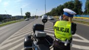 Na zdjęciu widać policjanta ruchu drogowego, przy motocyklu, który kontroluje prędkość pojazdów