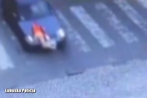 Stop klatka z filmu opublikowanego pod tekstem. Widać ciemny samochód osobowy na przejściu dla pieszych, na masce sylwetka dziecka.