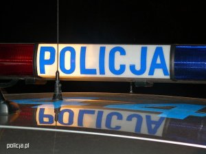 Zbliżenie policyjnego radiowozu na tzw. policyjną belkę z napisem Policja
