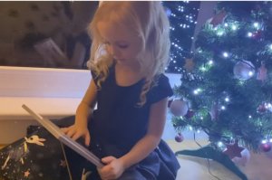 Przy choince siedzi mała dziewczynka, czyta list do Świętego Mikołaja