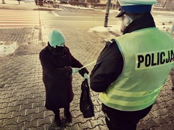 policjant przekazuje starszej kobiecie element odblaskowy, kobieta zakłada opaskę odblaskową
