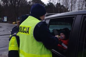policjant stoi przy samochodzie, okno pojazdu jest uchylone i widać w nim dziecko