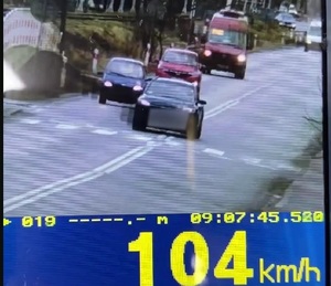 zdjęcie z policyjnego wideorejestratora, widać drogę, po której jadą pojazdy, na pierwszym planie pojazd w kolorze czarnym, na dole pasek z napisem 104 km/h