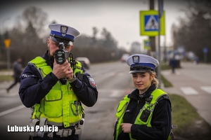 Na zdjęciu widać policjanta i policjantkę ruchu drogowego, mężczyzna trzyma w dłoni urządzenie do pomiaru prędkości pojazdów.