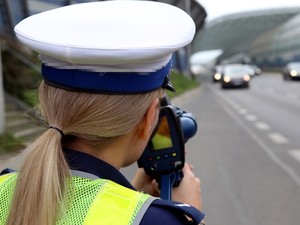 policjantka stoi przy ruchliwej drodze i mierzy prędkość wideorejestratorem