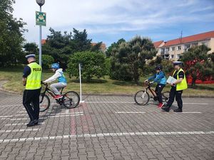 dzieci jada rowerami po miasteczku ruchu drogowego, policjanci oceniają tą konkurencję