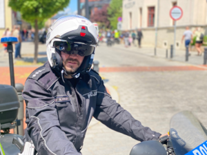 Na zdjęciu znajduje się policjant siedzący na motocyklu policyjnym, na głowie ma biały kask.