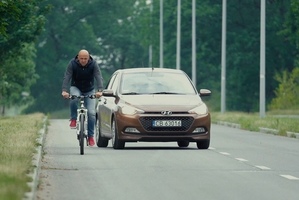 Na zdjęciu widać rowerzystę i wyprzedzający go samochód osobowy.