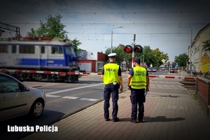 policjant i przedstawiciel straży kolei stoją obok przejazdu kolejowego
