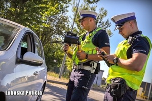 dwóch policjantów stoi obok szarego samochodu osobowego, w którym uchylona jest przednia szyba