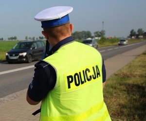 policjant w żółtej kamizelce z napisem POLICJA pełni służbę przy ruchliwej drodze