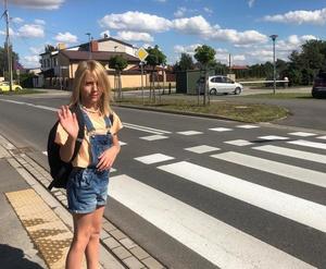 dziewczynka z tornistrem stoi przed przejściem dla pieszych i macha ręką