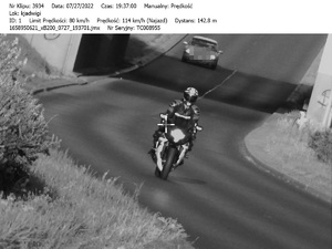 czarno białe zdjęcie z policyjnego wideorejestratora, na którym widać jadącego motocyklistę