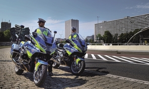 Dwóch policjantów stoi przy motocyklach oznakowanych, w tle widać wieżowce.