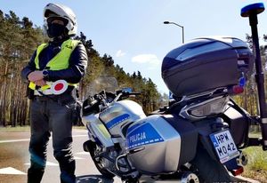 motocykl policyjny stoi przy drodze a obok policjant w kasku motocyklowym