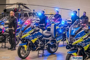 Nowe oznakowane motocykle BMW, obok nich policjanci, w oddali widać helikopter.