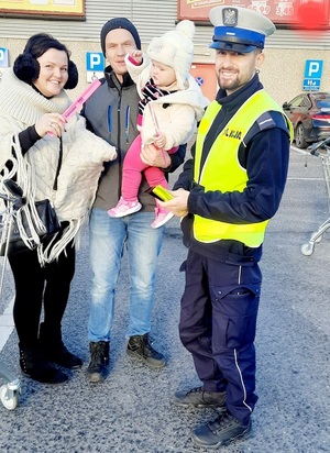 policjant wręcza rodzinie z dzieckiem opaskę odblaskową