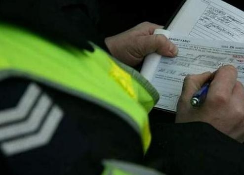 Na zdjęciu widać policjanta, który wypisuje mandat.