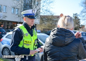 Na zdjęciu widać policjanta w białej czapce i przed nim stoi kobieta w czarnej kurtce.