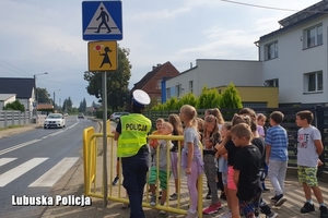 grupa dzieci stoi przed przejściem dla dzieci, obok stoi policjantka