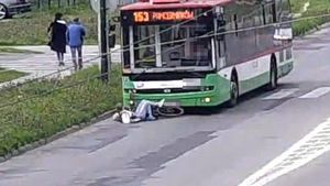 zielony autobus na jezdni, przed maska leżąca kobieta i rower