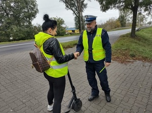policjant na chodniku przekazuje elementy odblaskowe młodej kobiecie