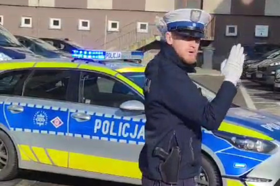 policjant kierujący ruchem na tle oznakowanego radiowozu, policjant ma białe rękawiczki
